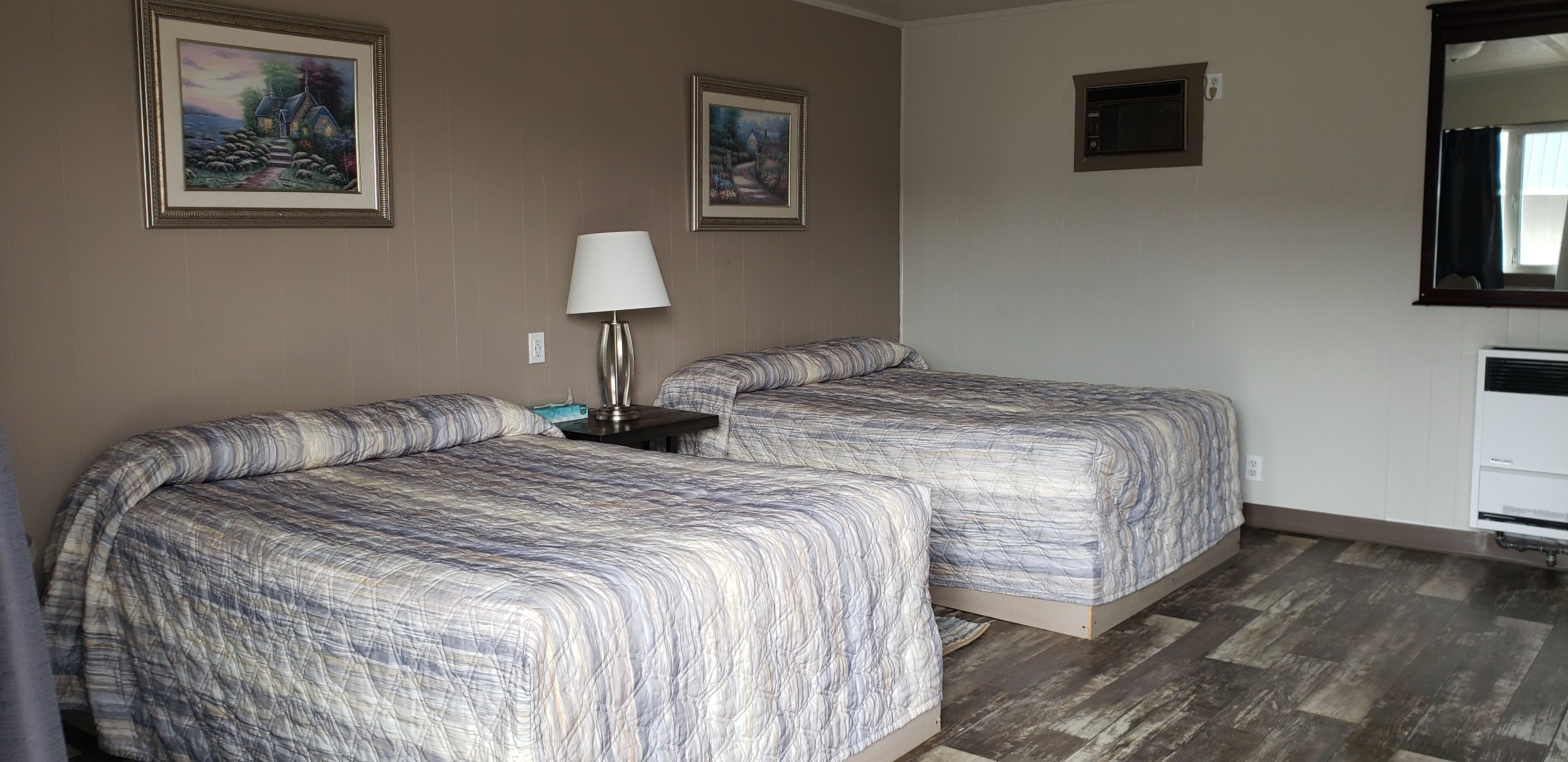 Habitación de hotel con dos camas, una lámpara, una mesita pequeña y dos cuadros en la pared.