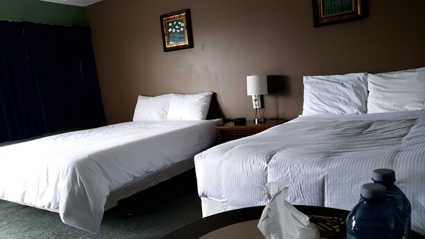 A hotel room with two beds, a bedside table with a lamp, a water bottle, and a tissue box.