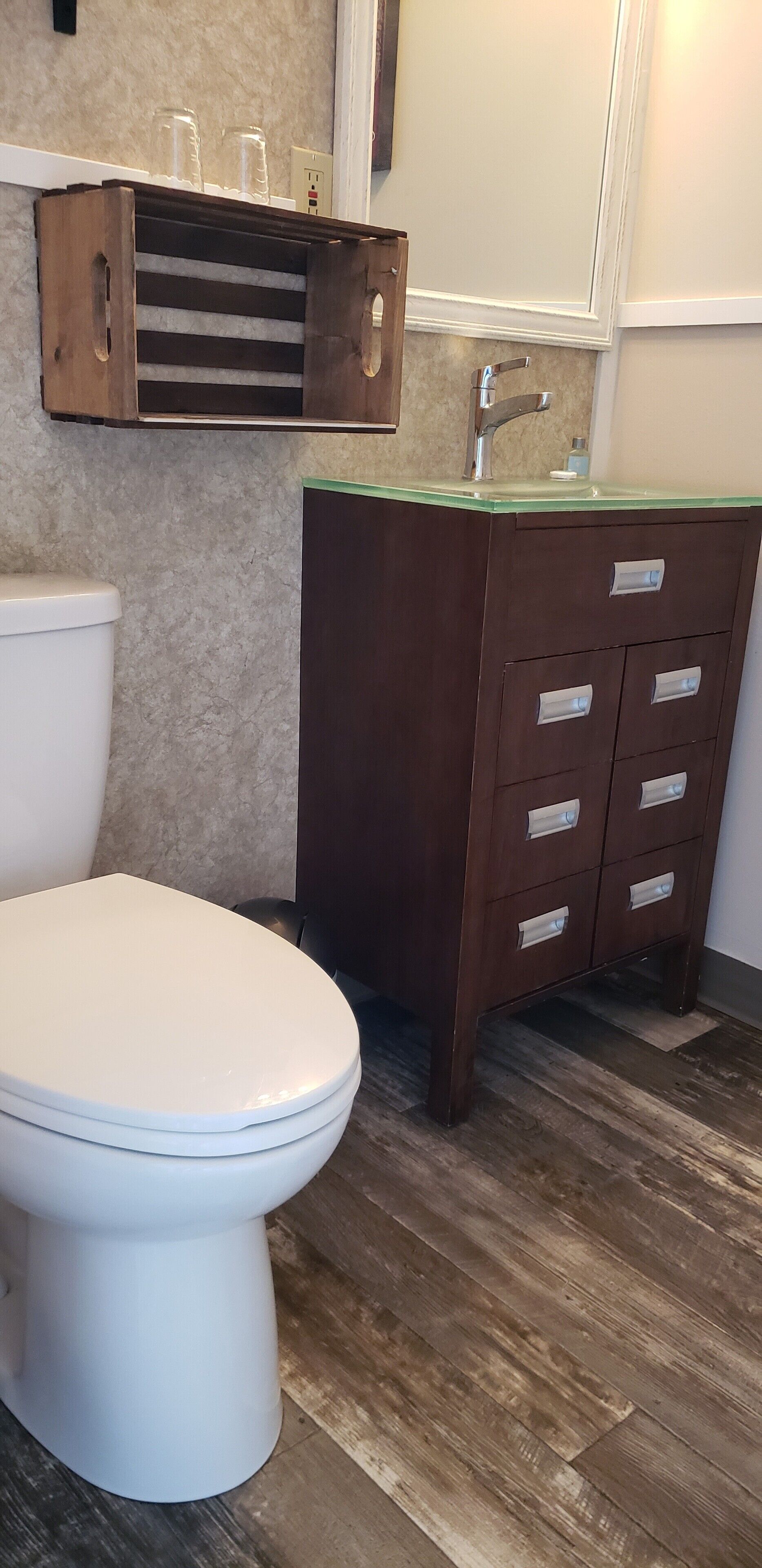 Een badkamer met een wit toilet, een houten wastafelmeubel met lades en een glazen plank boven de wasbak.