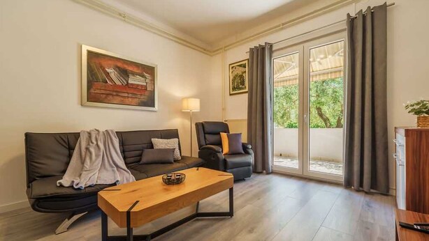 A modern living room with a sofa, armchair, and coffee table, a painting on the wall, and a sliding glass door leading to an outdoor area. - Apartment Juranic with spacious Terrace (Krk)