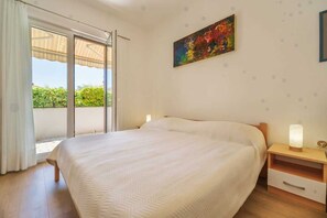 A bedroom with a bed, a nightstand, a lamp, a painting, and a sliding glass door to a balcony. - Apartment Juranic with spacious Terrace (Krk)