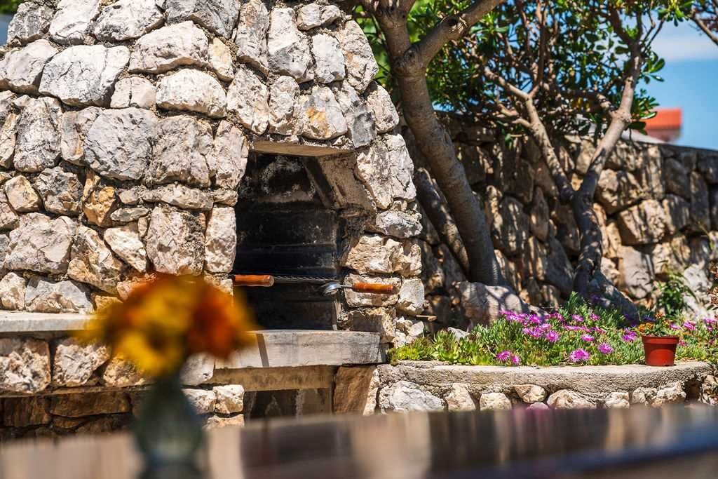 A stone building with a chimney, surrounded by greenery and flowers.
