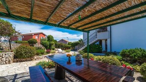 An outdoor patio with a wooden table and benches, surrounded by stone flooring and greenery. - Apartment Juranic with spacious Terrace (Krk)