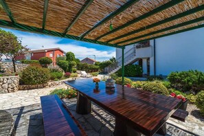 An outdoor patio with a wooden table and benches, surrounded by stone flooring and greenery. - Apartment Juranic with spacious Terrace (Krk)