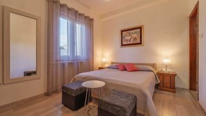 A bedroom with a bed, two bedside tables, a window with curtains, a painting on the wall, and a small round table. - Apartment Juranic with spacious Terrace (Krk)
