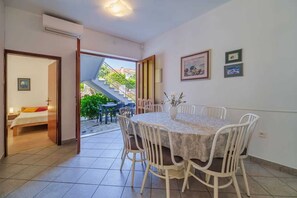 Un coin repas avec une table ronde et des chaises, un petit vase avec des fleurs et un escalier menant à l’extérieur.