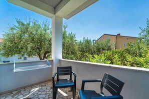 A balcony with two chairs, a metal grill, and a view of greenery and buildings. - Apartment Juranic with spacious Terrace (Krk)