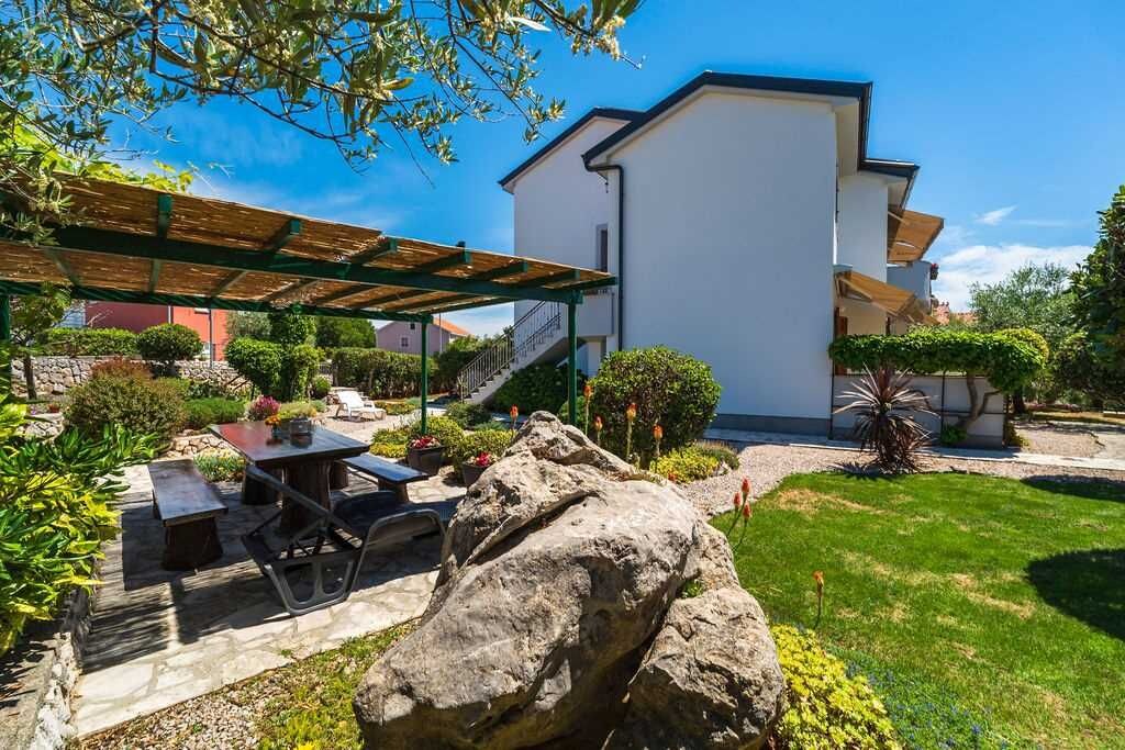 Un bâtiment moderne doté d’un patio couvert, d’un chemin en pierre et d’un jardin bien entretenu.