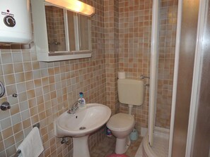 A bathroom with a white sink, toilet, and shower. There is a mirror above the sink and a Koncar heater on the wall. - Apartment Dragica 2 on the ground floor (Malinska)