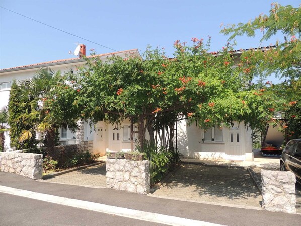 A white building with a stone wall entrance, a covered patio, and a parked car. - Apartment Dragica 2 on the ground floor (Malinska)
