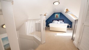 A bedroom with a bed, a nightstand, a desk, and a chair. There is a window with blinds and a painting on the wall.