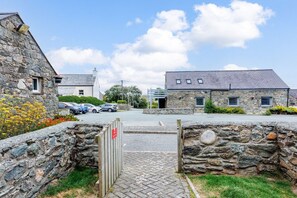 A stone building with a paved entrance, a small window, and a red sign. - Bwthyn Branwen: Accessible, pet-friendly cottage, Aberffraw (Ty Croes)