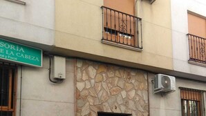 Un edificio con fachada de piedra, una puerta negra y un pequeño balcón con barandilla metálica.