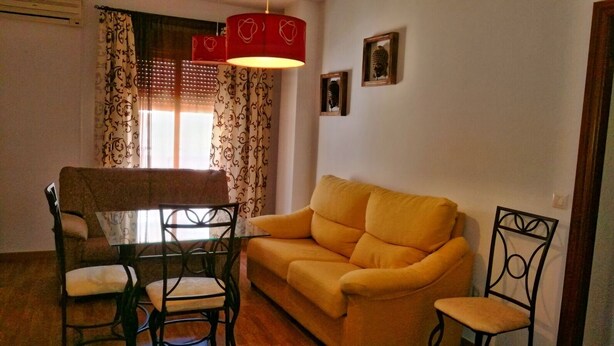 Una sala de estar con un sofá amarillo, una mesa de comedor con sillas y una lámpara roja.
