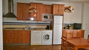 Cocina compacta con armarios de madera, lavadora, refrigerador, microondas y comedor con mesa y sillas.