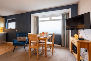 A room with a dining table, chairs, a TV, a window, and a view of the outdoors. - Bay View: A two bed, pet-friendly holiday apartment in Rhosneigr (Rhosneigr)