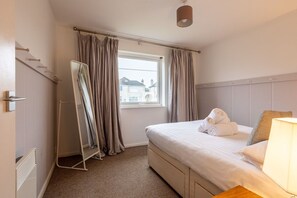 A hotel room with a bed, a window with curtains, a radiator, and a bedside lamp. - Bay View: A two bed, pet-friendly holiday apartment in Rhosneigr (Rhosneigr)