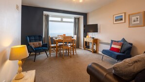 A modern living room with a dining area, a flat-screen TV, and a view of the sea.