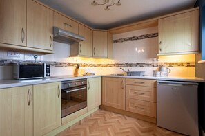 A kitchen with wooden cabinets, a microwave, an oven, and a dishwasher. - Bay View: A two bed, pet-friendly holiday apartment in Rhosneigr (Rhosneigr)