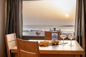 A table with snacks, a bottle, and glasses, set against a view of the sea. - Bay View: A two bed, pet-friendly holiday apartment in Rhosneigr (Rhosneigr)