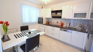 Een moderne keuken met witte kastjes, een zwart aanrechtblad en een eethoek met een geruit tafelkleed.