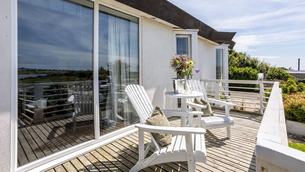 A balcony with white chairs and a table, large windows, and a view of the landscape. - Owain’s Lake View : Pet-Friendly 1‑Bed Lakeside Apartment with Maelog Lake Views | Managed by Angles (Ty Croes)