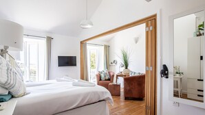 A bedroom with a large bed, a desk, a chair, and a TV. There is a wooden door leading to another room. - Owain’s Lake View : Pet-Friendly 1‑Bed Lakeside Apartment with Maelog Lake Views | Managed by Angles (Ty Croes)