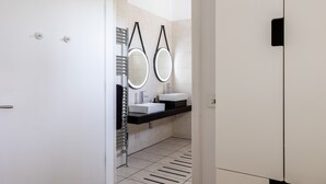 A modern bathroom with a white door, a towel rack, two sinks with black countertops, and two wall-mounted mirrors. - Owain’s Lake View : Pet-Friendly 1‑Bed Lakeside Apartment with Maelog Lake Views | Managed by Angles (Ty Croes)