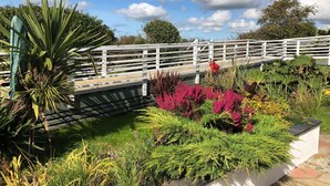 A garden with a white fence, various plants, and a pathway. - Owain’s Lake View : Pet-Friendly 1‑Bed Lakeside Apartment with Maelog Lake Views | Managed by Angles (Ty Croes)