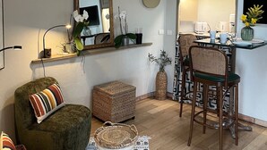 En kompakt bolig med tekøkken, spiseplads med to barstole, spejlvæg og et lille rundt ur.