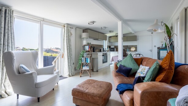 A spacious living room with a large window, a sofa, a chair, and a small ottoman. - Bryn Bach: Romantic 1-Bed Cottage with Hot Tub in Llanfaelog | Managed by Anglesey Holiday Lettings (Ty Croes)