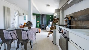 A modern kitchen with a dining area, featuring a checkered tablecloth, chairs, and a stove. - Bryn Bach: Romantic 1-Bed Cottage with Hot Tub in Llanfaelog | Managed by Anglesey Holiday Lettings (Ty Croes)