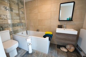 Modern bathroom with shower over bath, sink and toilet, one-bedroom romantic retreat in Llanfaelog, Anglesey - Bryn Bach: Pet-friendly cottage on the Isle of Anglesey (Ty Croes)