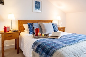 A neatly made bed with a blue blanket, two bedside tables with lamps, a red kettle, and a book.