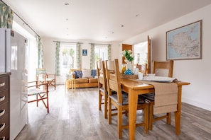 A modern kitchen with wooden cabinets, a dining table with chairs, a sofa with cushions, and a map on the wall.