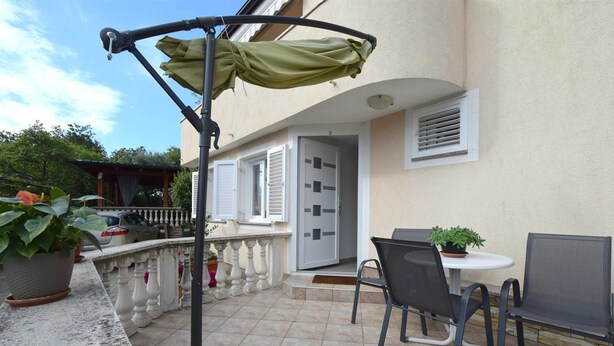 Un patio al aire libre con una mesa, sillas, una planta en maceta y un paraguas verde.