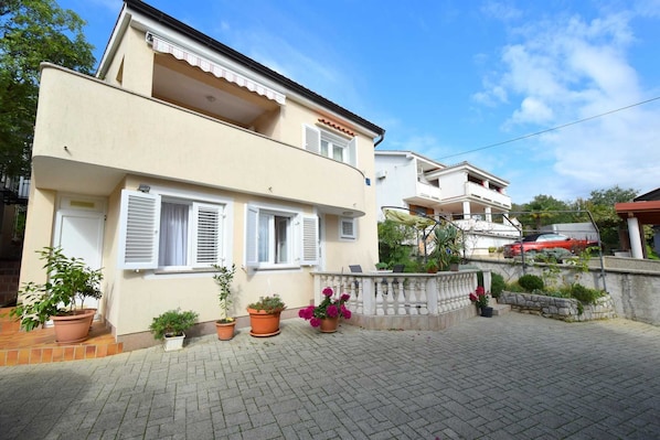 A two-story building with a balcony, potted plants, and a paved driveway.