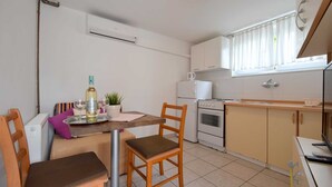 Una cocina compacta con comedor, muebles blancos, estufa y ventana con cortinas.