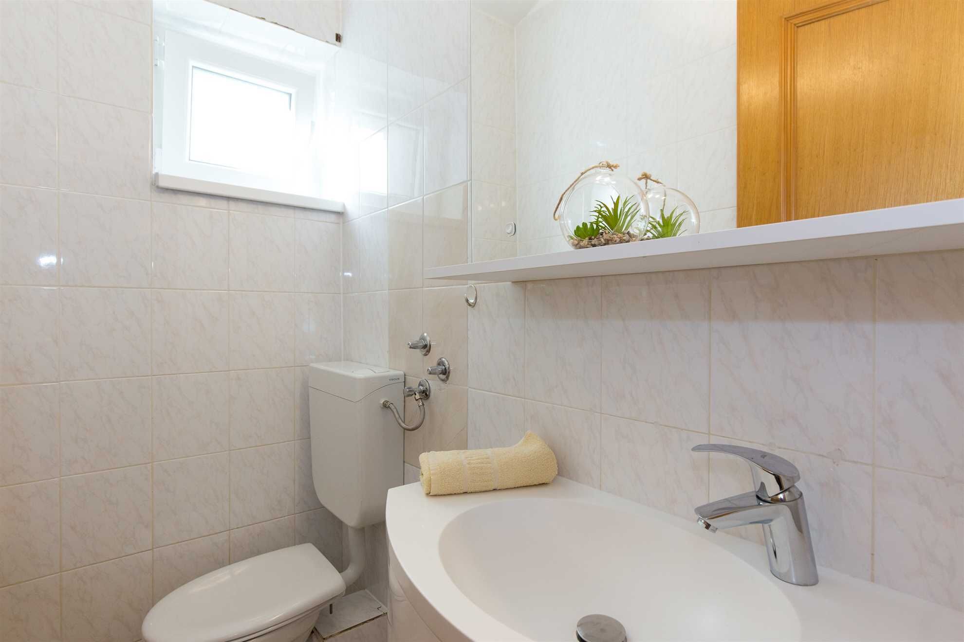 A bathroom with a toilet, a sink with a modern faucet, and a shelf with a plant.