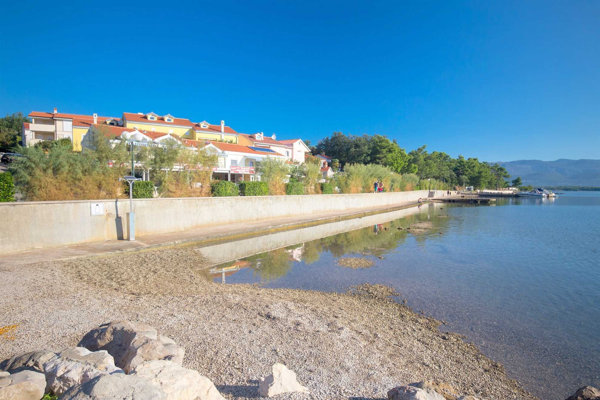 A waterfront area with buildings, a calm water body, and a rocky shoreline.