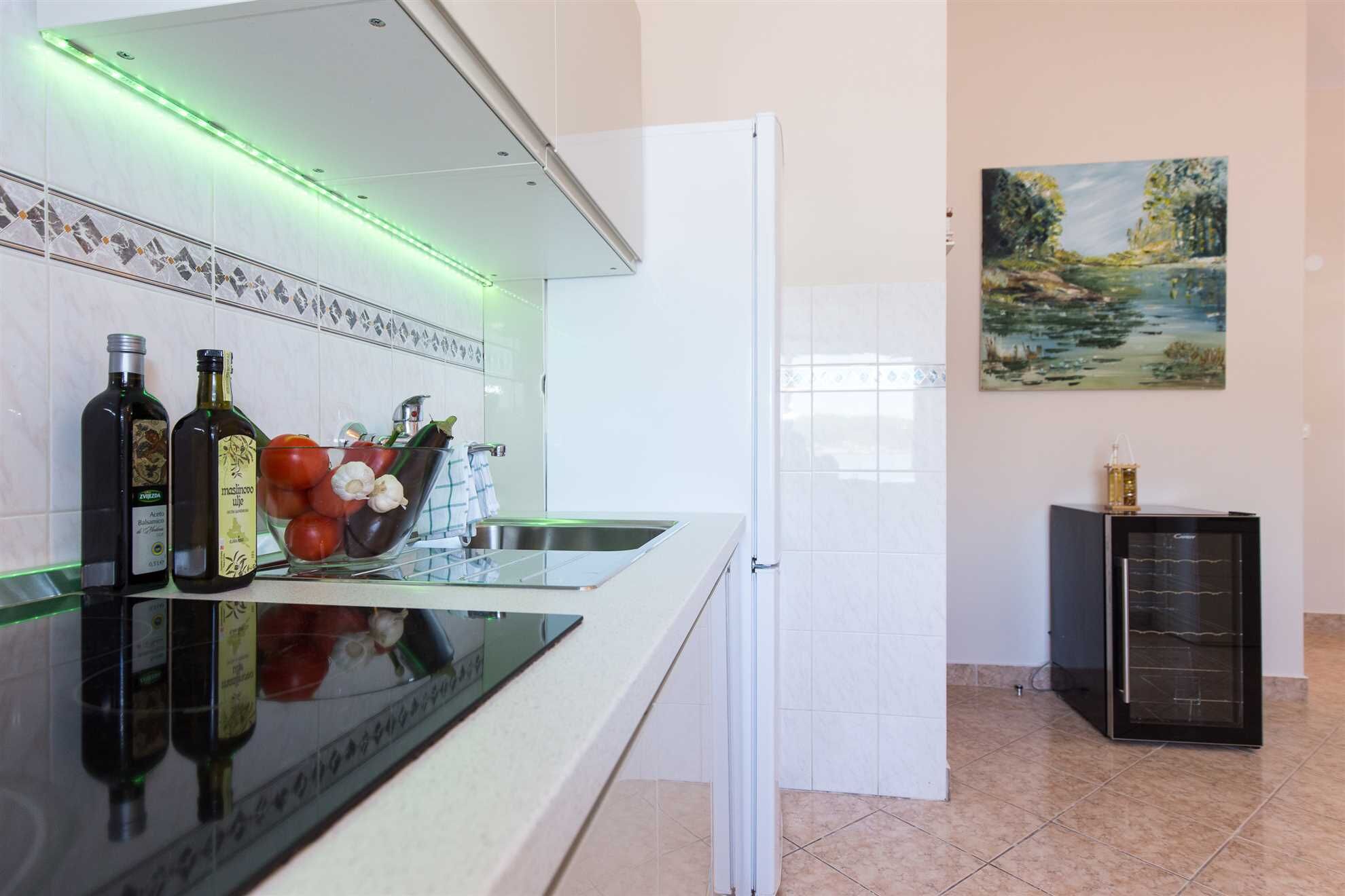 Eine Küche mit einer Glas Arbeitsplatte, zwei Weinflaschen, einer Schüssel mit Gemüse und einem Bild an der Wand.