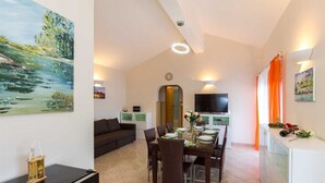 A dining area with a table set for four, a sofa, a TV, and artwork on the walls. - Apartment Tamaris D with Seaview (Čižići)