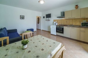 A compact living space with a sofa, a dining table with a floral tablecloth, a small kitchen with a stove, microwave, and cabinets. - Apartment Anka 1 with Terrace (Krk)
