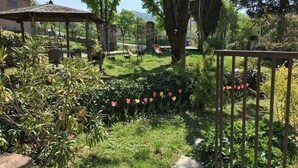 Un jardín con un pabellón, una cerca de metal y una variedad de plantas y flores.