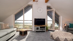 Amplia sala de estar con televisor grande, sofá cómodo y vista a la playa a través de ventanas grandes.