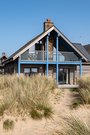 A modern house with a stone facade, blue accents, and a large glass balcony. - Niwl Y Mor: Beachfront Rhosneigr cottage for 6 guests (Rhosneigr)