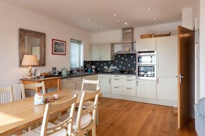 A modern kitchen with white cabinets, a wooden dining table, and a built-in oven.