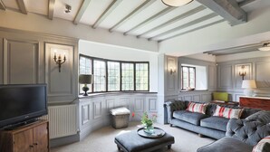 Un salon avec un téléviseur posé sur un meuble en bois, un canapé gris et une fenêtre donnant sur un paysage verdoyant.