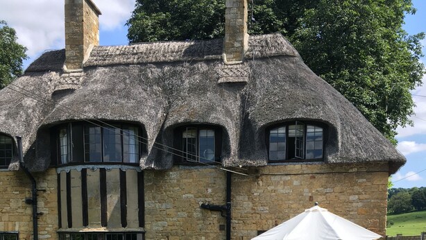 Une maison en pierre avec un toit de chaume, un chemin de pierre et un jardin où poussent des plants de lavande.