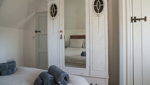 Une chambre à coucher avec un grand lit, une armoire blanche à deux portes et un miroir.
